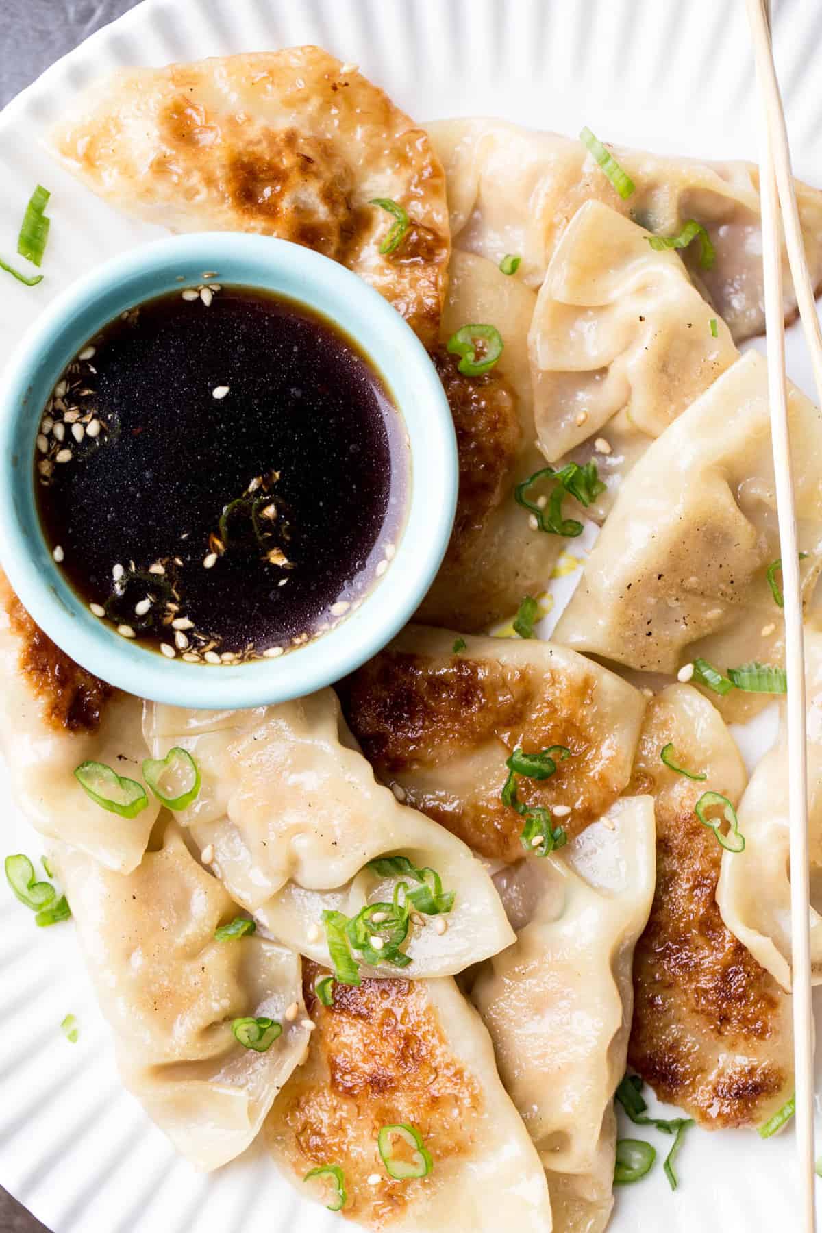 Chicken gyoza recipe on a plate topped with greens and next to a bowl of gyoza sauce.