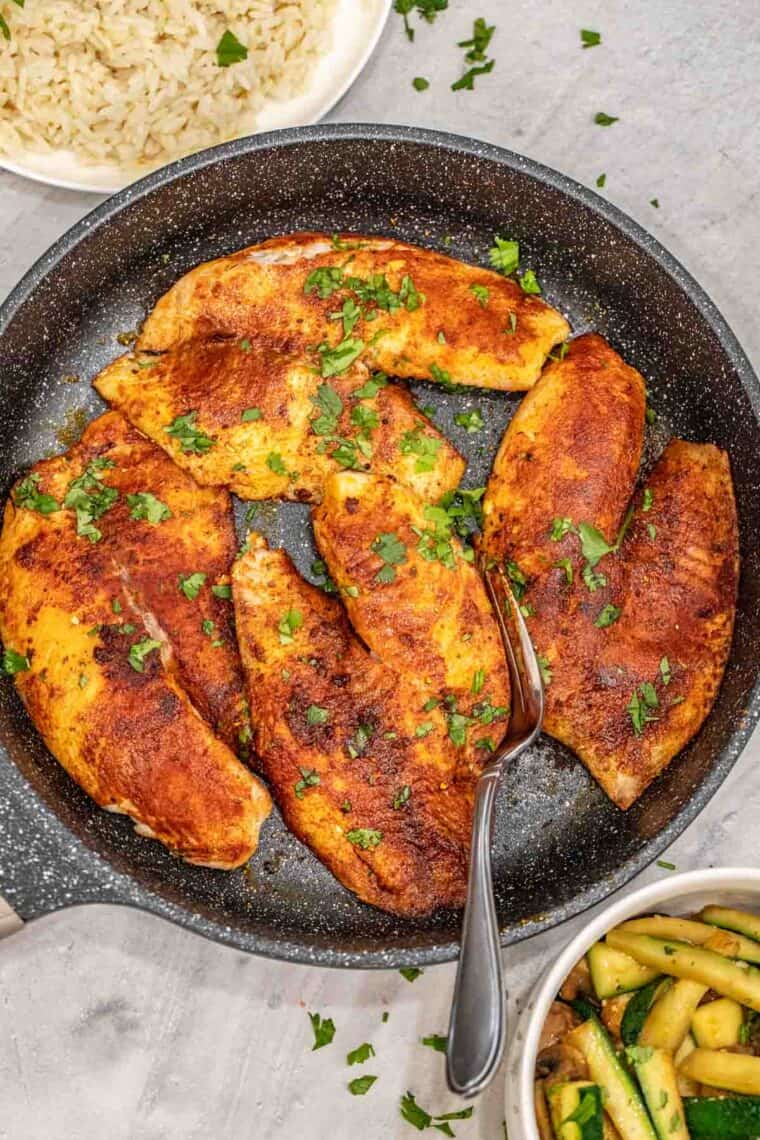 Blackened tilapia fish recipe in a skillet with lemon and fresh herbs.