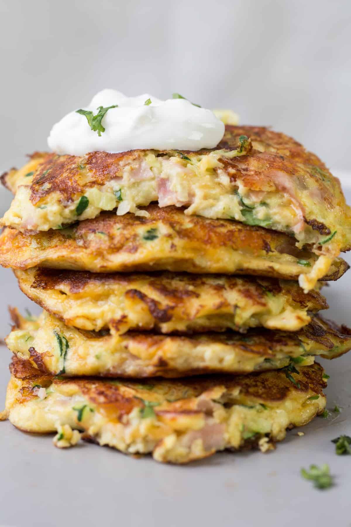 Zucchini fritter stacked on top of each other with a dallop of sour cream on top.