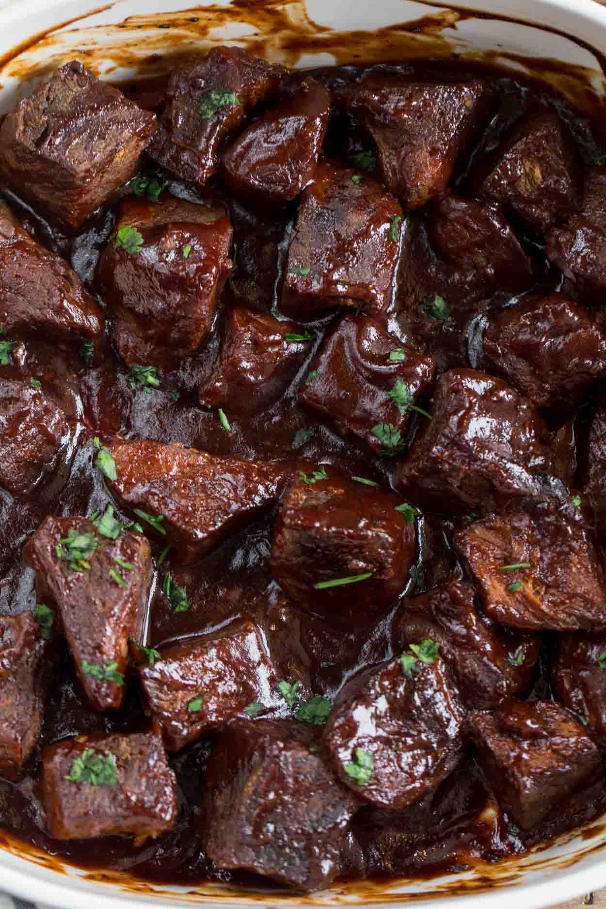 Meat chunks in a barbecue sauce topped with fresh greens.