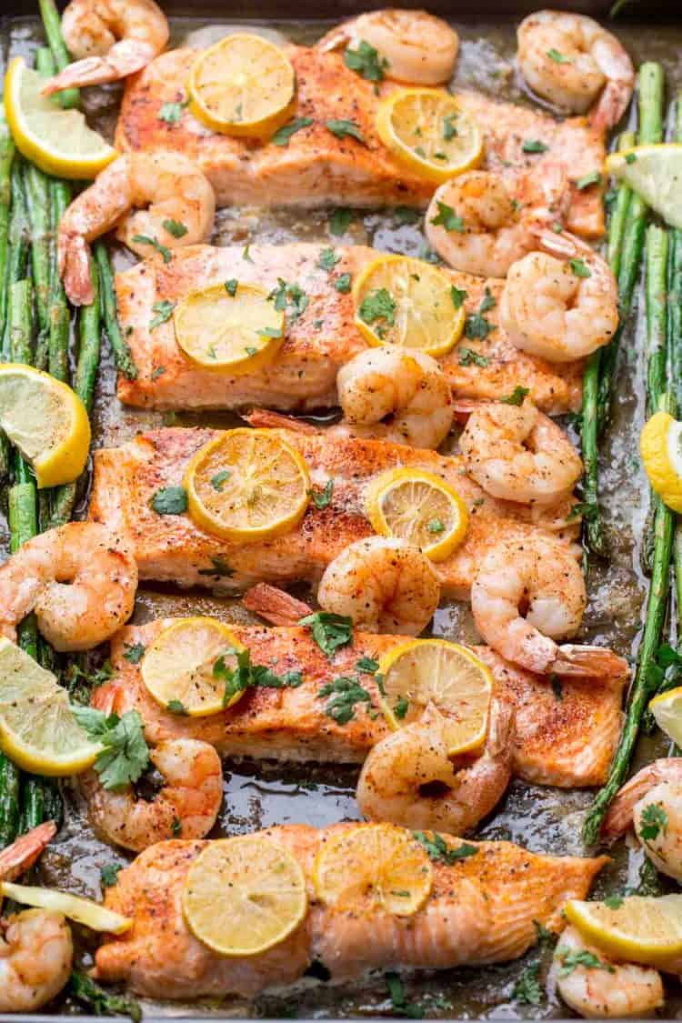 One pan baked salmon shrimp salmon recipe with asparagus, lemons and fresh herbs on a baking sheet.