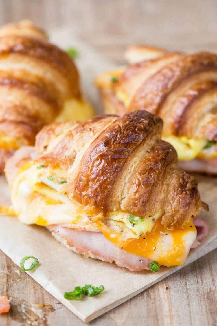 Homemade reakfast croissant sandwich recipe with ham, egg and cheese, on a cutting board.
