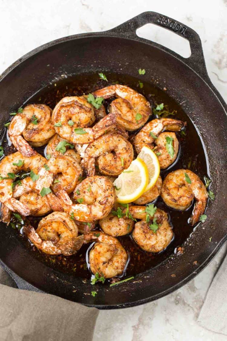 Garlic butter sautéed shrimp in a skillet topped with fresh greens and lemon juice.