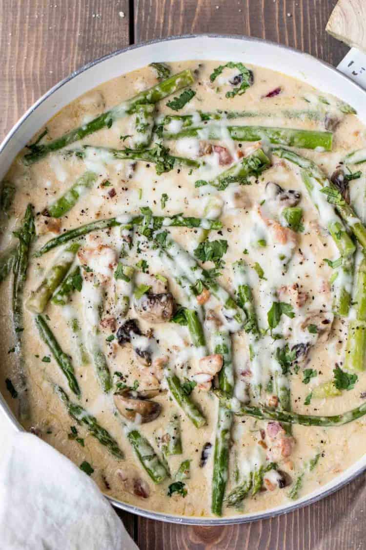 Asparagus in creamy mushroom sauce with bacon and mushrooms in a skillet.