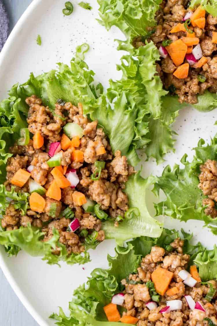 Chicken lettuce wraps made with ground chicken, peanut butter, soy sauce topped with cucumber, carrots and radishes on a plate.