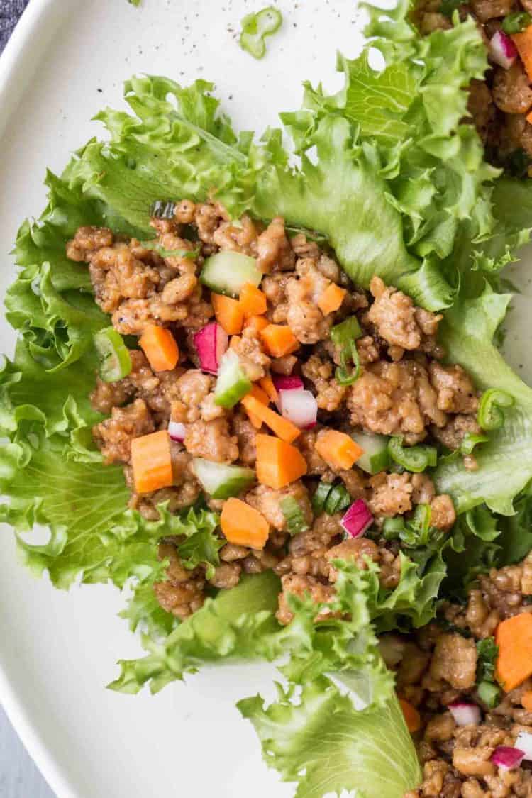 A close up picture of lettuce wraps, lettuce filled with ground chicken tossed in a peanut butter sauce on a plate.