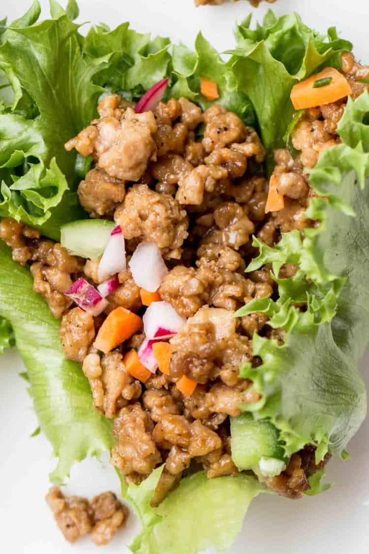 Close up picture of Chicken Lettuce Wraps topped with carrot, radish, and cucmbers.