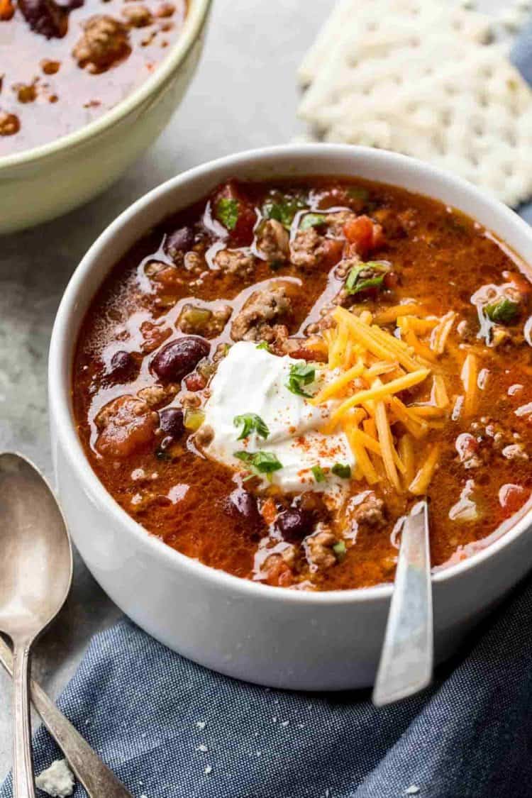 Beef chili recipe in a bowl topped with sour cream and cheese with crackers on the side.