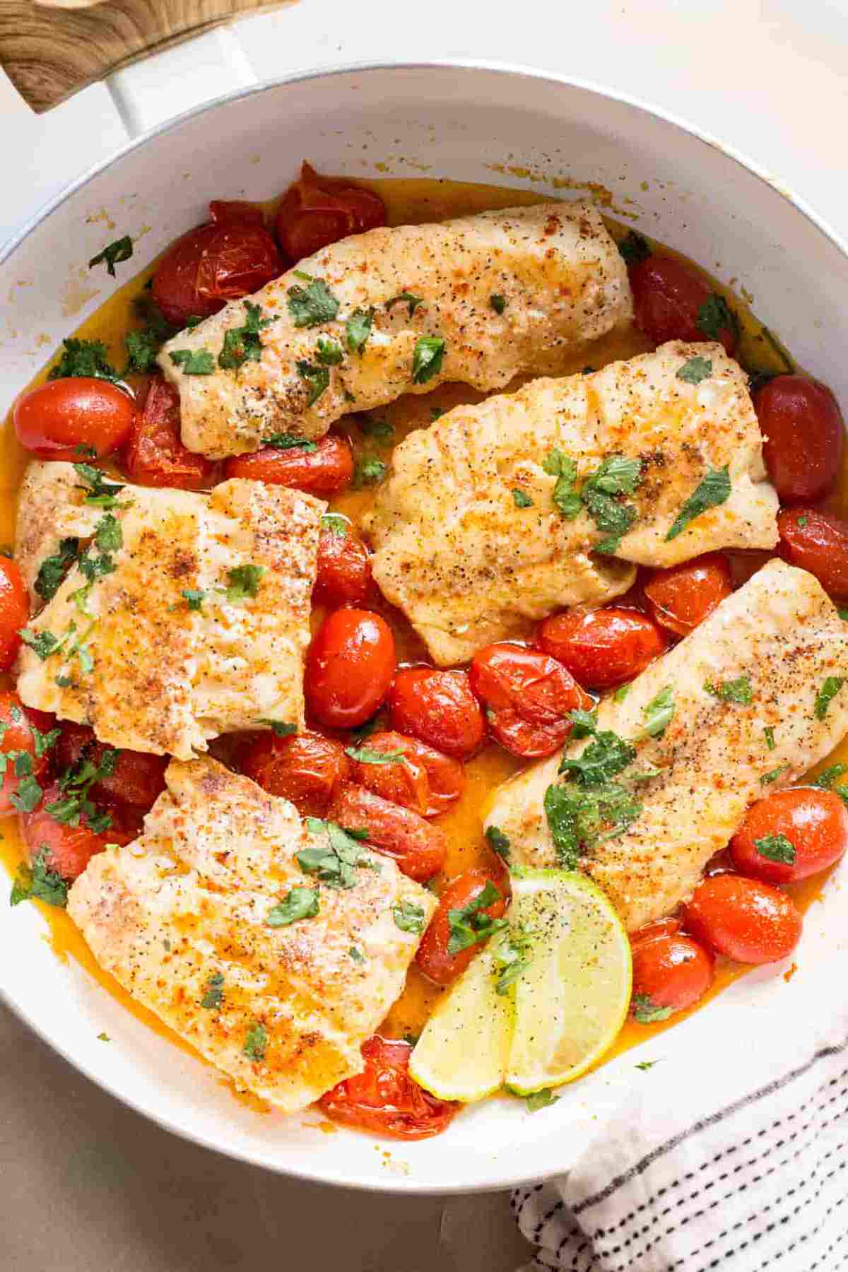 Cod fish recipe in a skillet with tomatoes, and freshly chopped herbs.