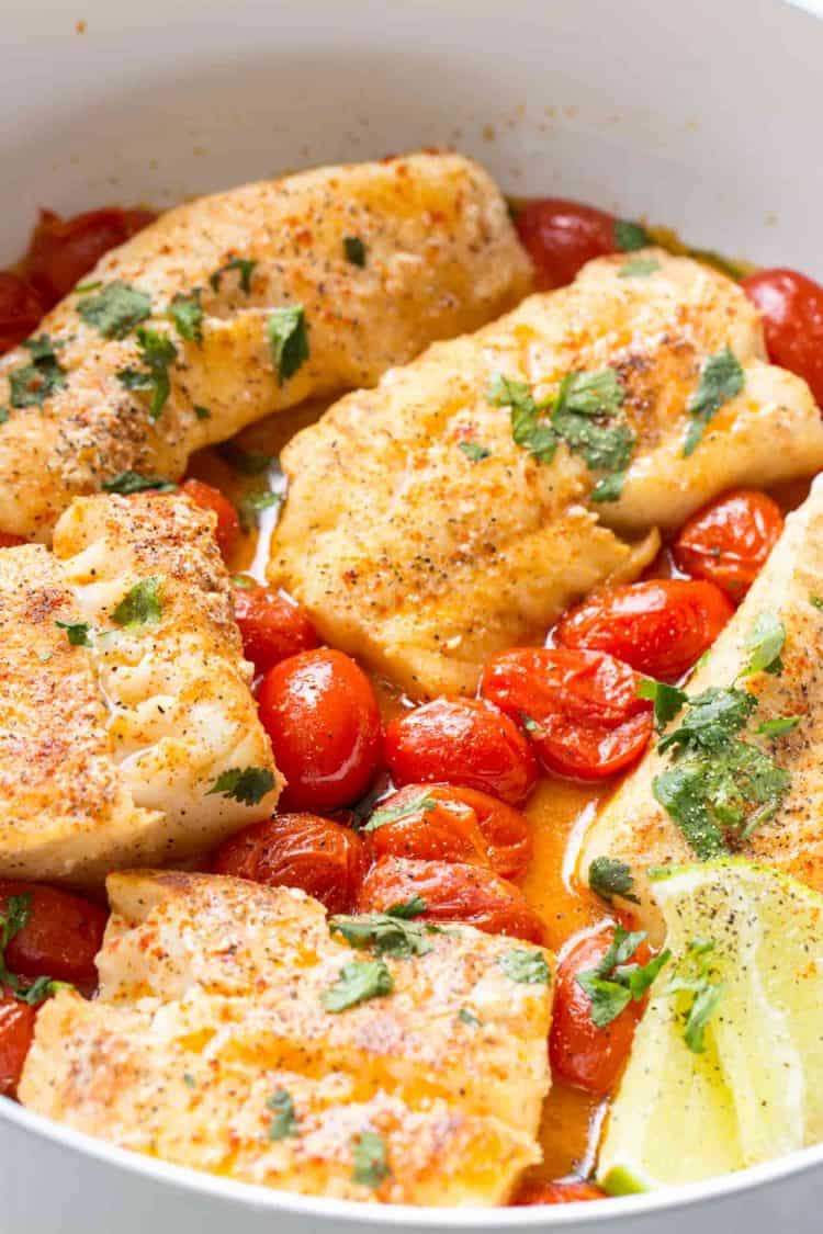 Upclose picture of how to cook a simple cod recipe with tomatoes and sauce.