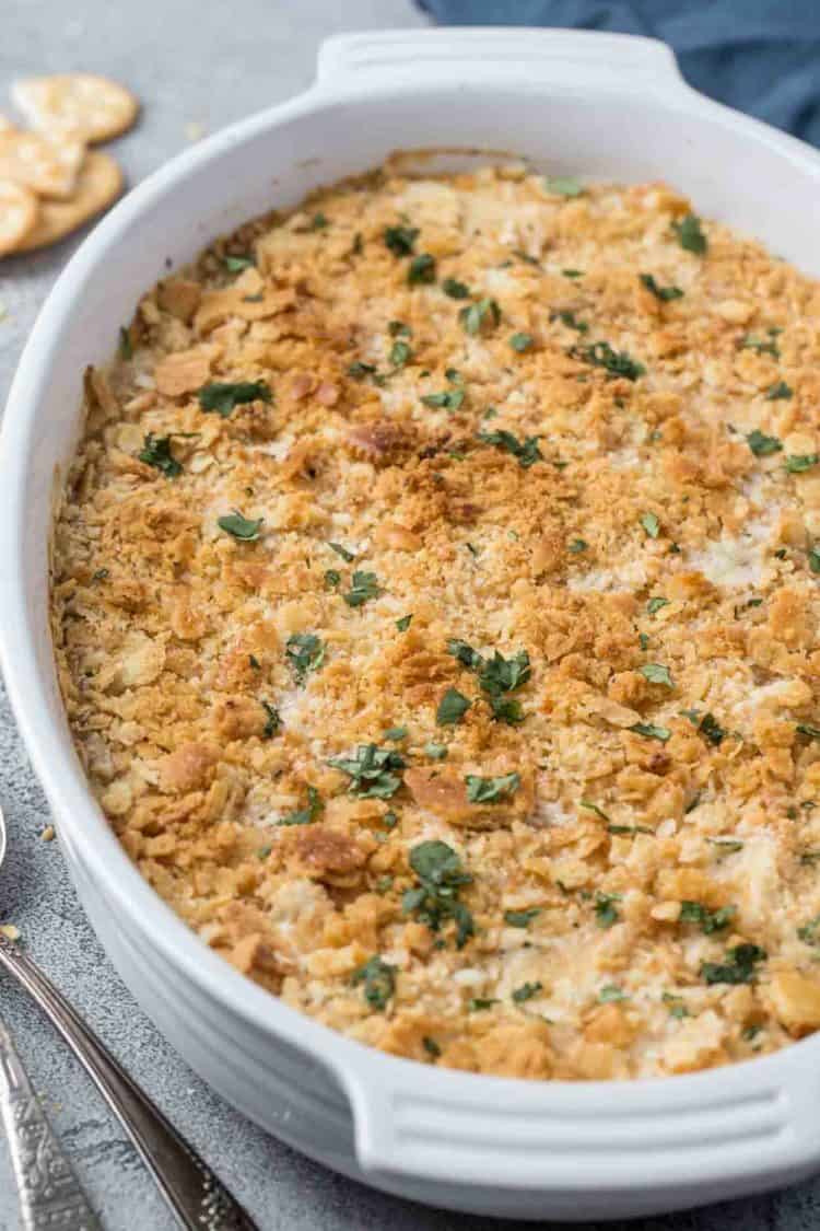 Creamy poppy seed chicken in a casserole dish topped with crackers and fresh greens. 