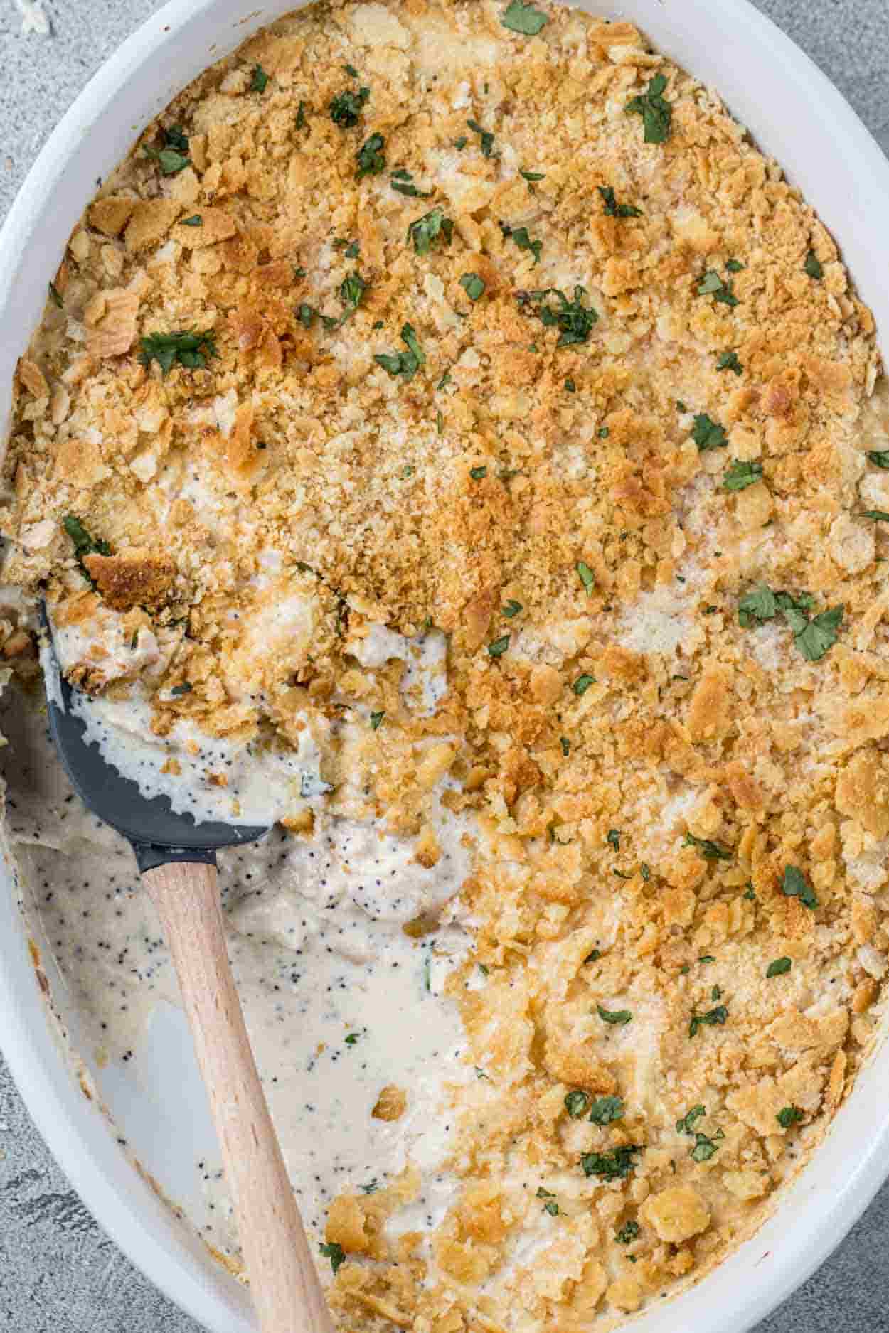 Poppy seed chicken in a casserole dish with a spatula, topped with greens.