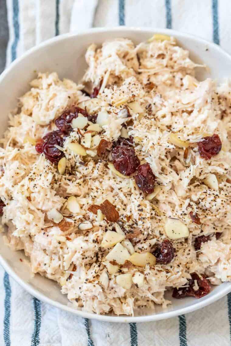 Chicken salad with sliced almonds and cranberries in a white bowl topped with black pepper. 