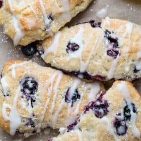 Four blueberry scones, laid out next to each other, drizzled with glaze.