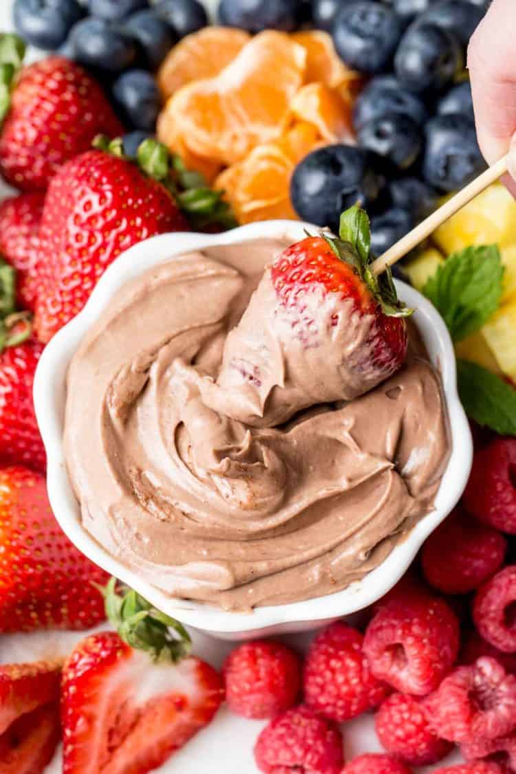Strawberry dipped in chocolate dip with fresh fruit around it.