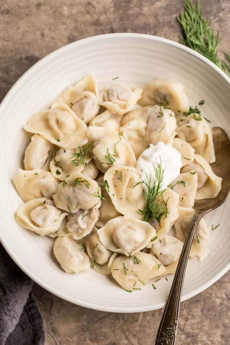 Pelmeni recipe with a meat filling in a bowl with fresh dill and sour cream.