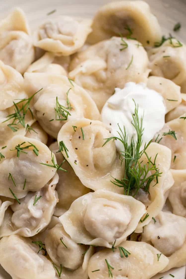 Russian dumplings with a meat filling in a bowl with fresh chopped dill and sour cream.