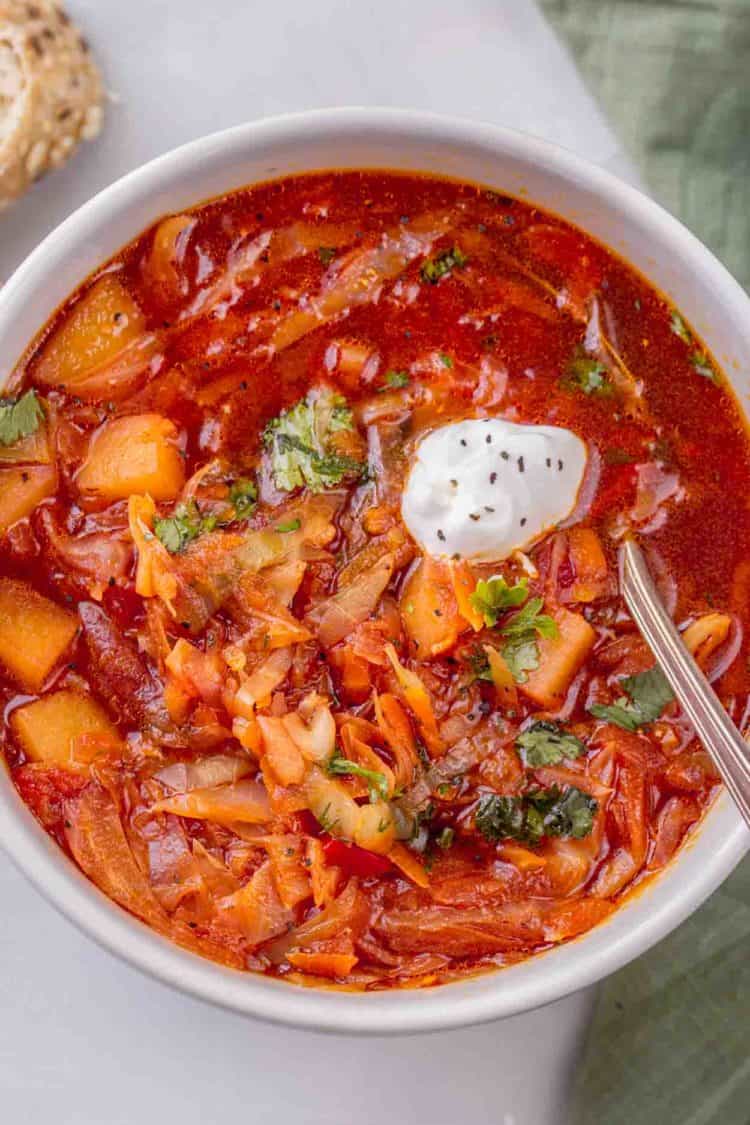 Borscht recipe in a bowl oven topped with fresh greens and sour cream.