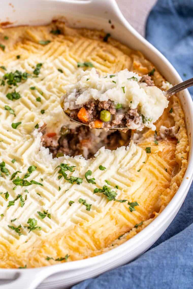 Easy hearty pie in a casserole dish with a spoon of pie topped with fresh greens.