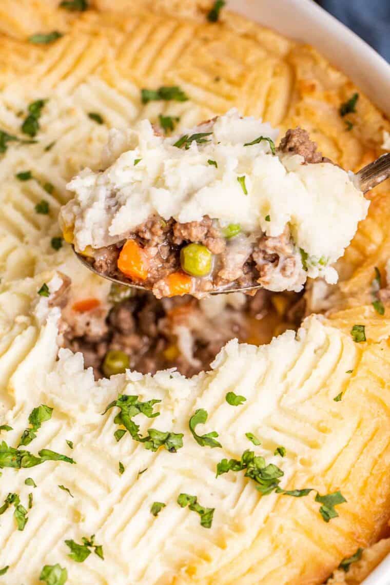 Shepherd's pie in a casserole dish with a spoon and topped with fresh greens.