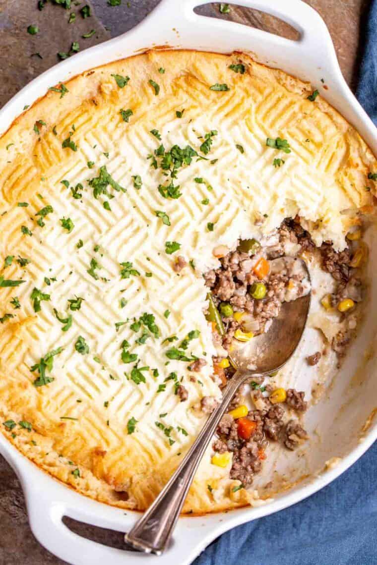 Shepherd's pie in a casserole dish with a spoon, topped with fresh greens.