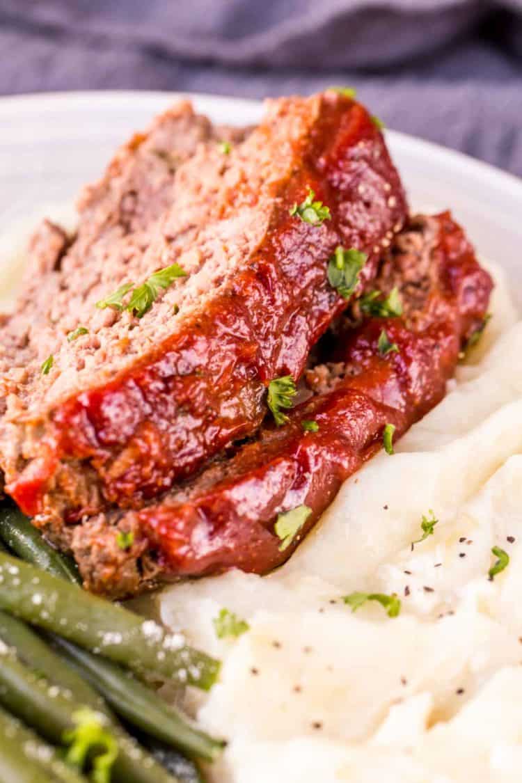 Sliced meatloaf on a bed of mashed potatoes with green beans in a plate.