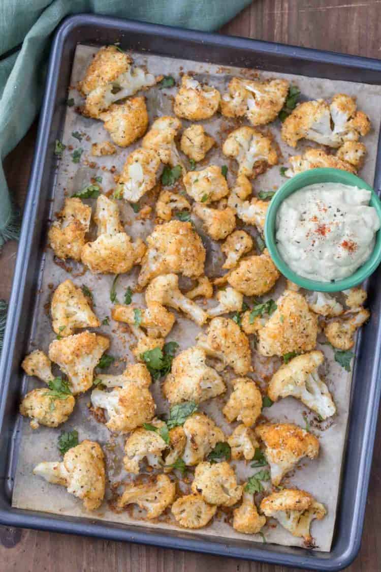Crispy cauliflower topped with fresh greens on a baking sheet with avocado dip.