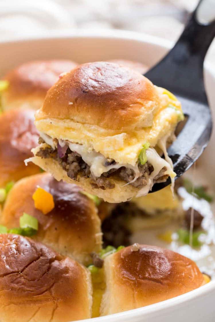 Breakfast sliders recipe in a casserole dish with a slider on a spatula.