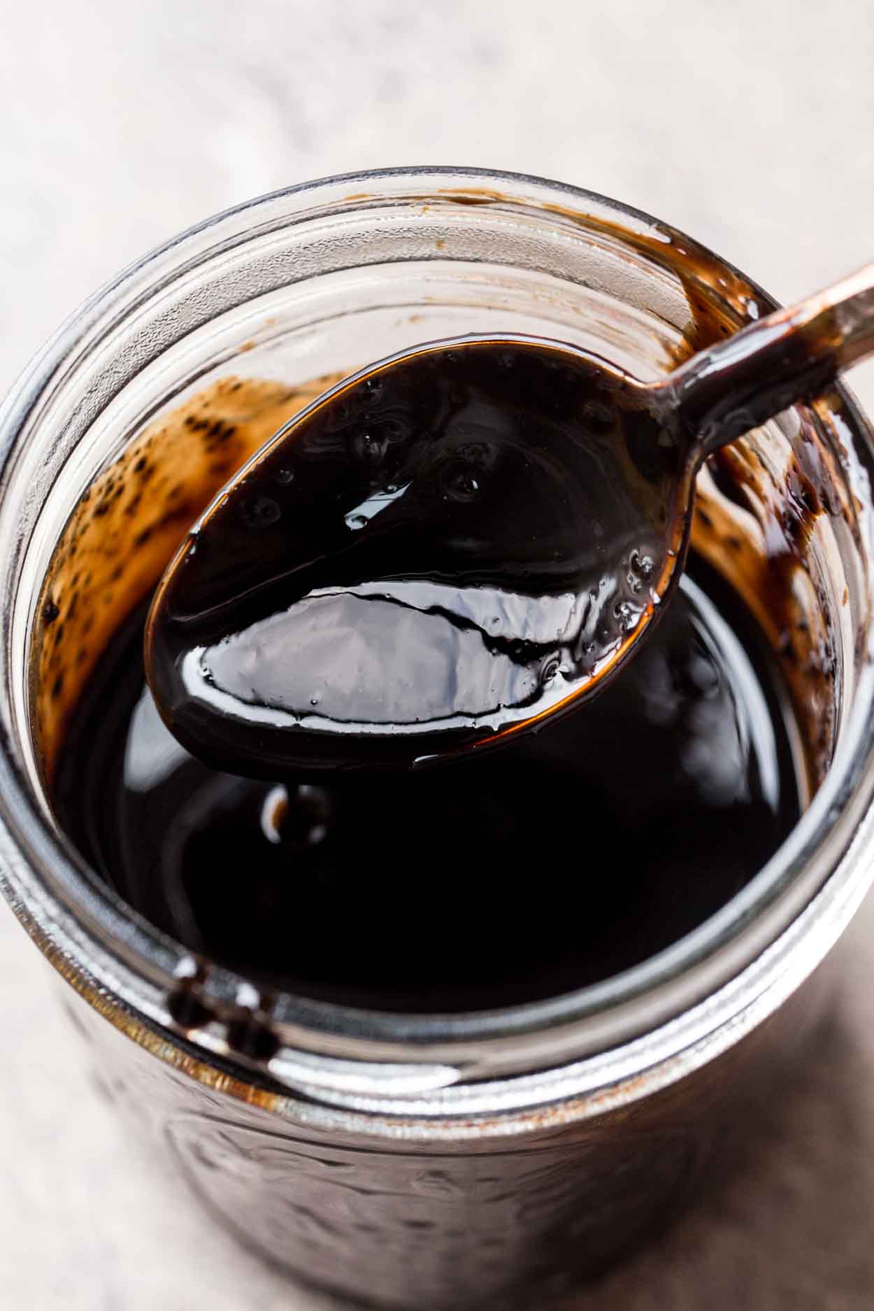 A jar of balsamic glaze with a spoon to show the consistency. 
