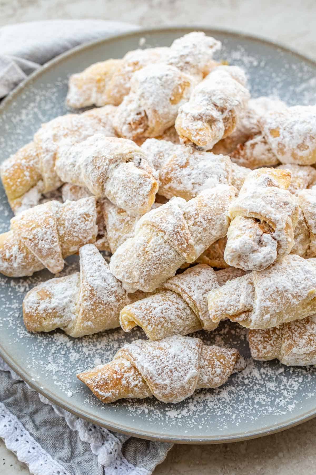 Sugary rugelach cookies topped with powdered sugar in a blue plate. 