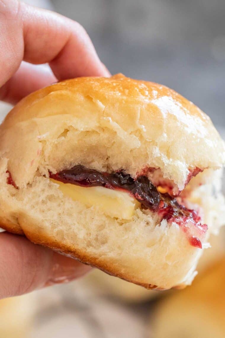 Dinner roll with jam and butter being held. 