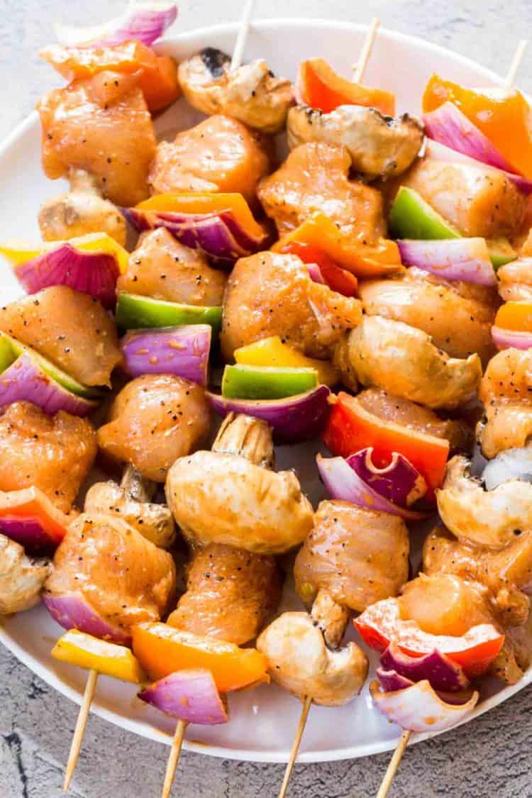 Chicken kabobs on skewers with mushrooms and vegetables on a plate with sliced lemons.