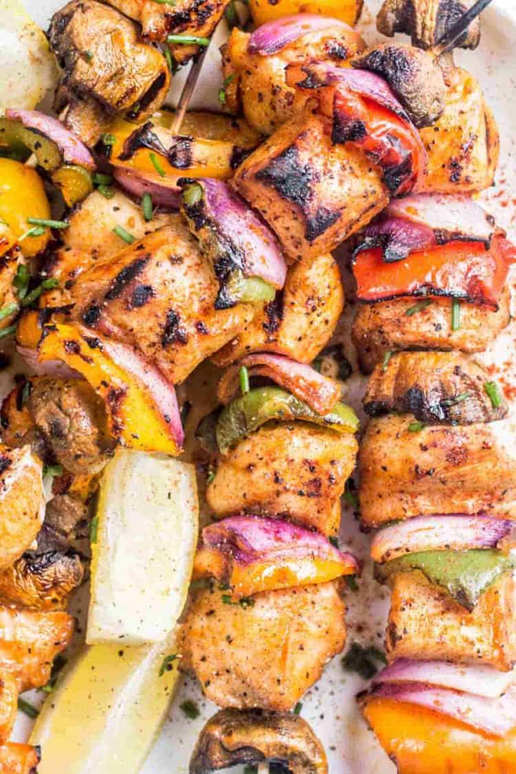 Grilled chicken on skewers with vegetables next to lemons on a plate.