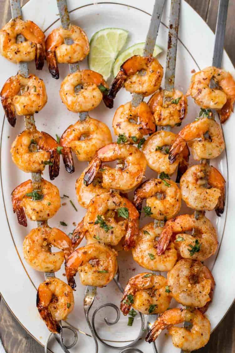 Grilled shrimp on skewers on a plate with lime and fresh greens.