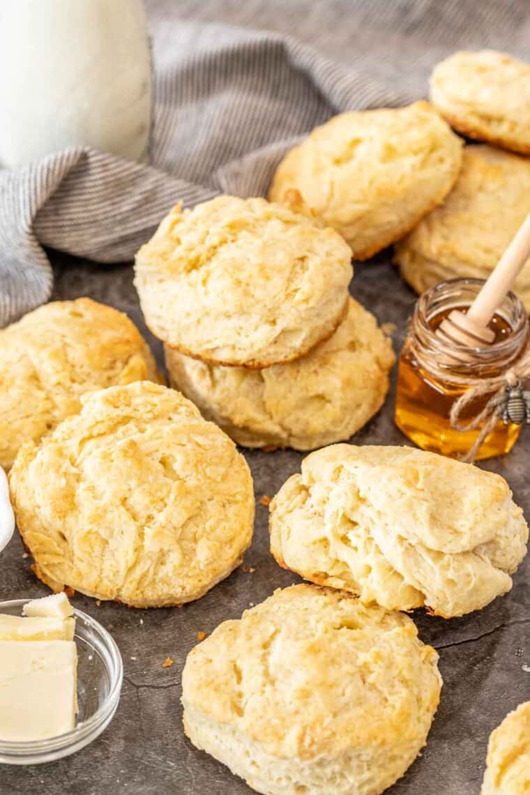 Biscuits laid out next to a bowl of butter and jar of honey. 