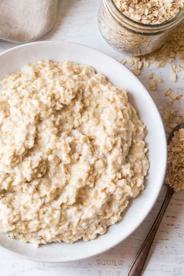 A bowl of simple oatmeal next to a jar of oatmeal and a spoon full of oats.