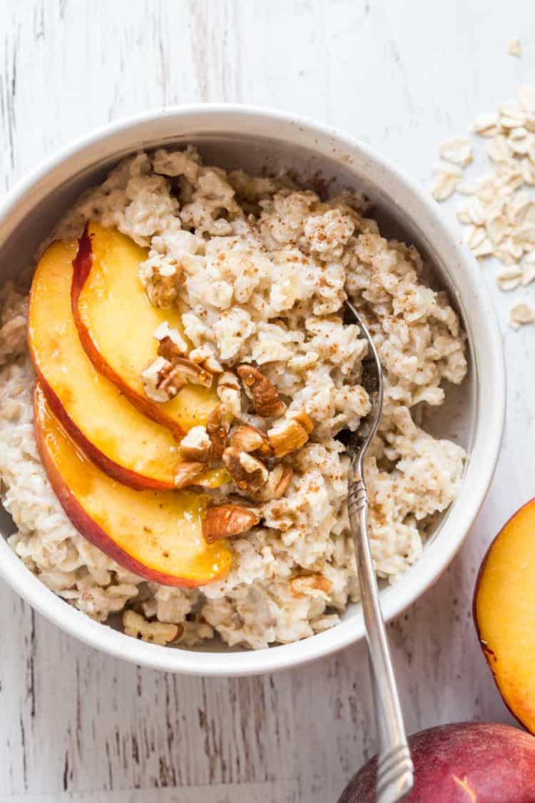 Oatmeal made with peaches and walnuts in a bowl with a spoon. 