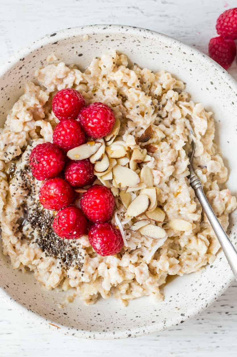 Raspberries, chai seeds and almonds with cooked oatmeal in a bowl next to raspberries.