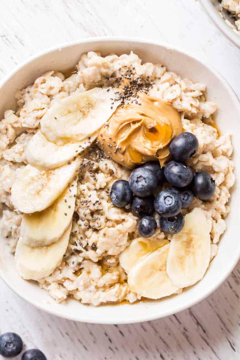 A bowl of homemade oatmeal with bananas, blueberries and peanut butter on top.