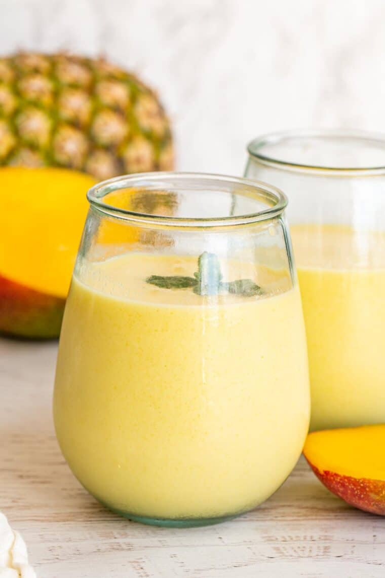 Smoothie in glass cups with pineapple and fresh mango on the side.