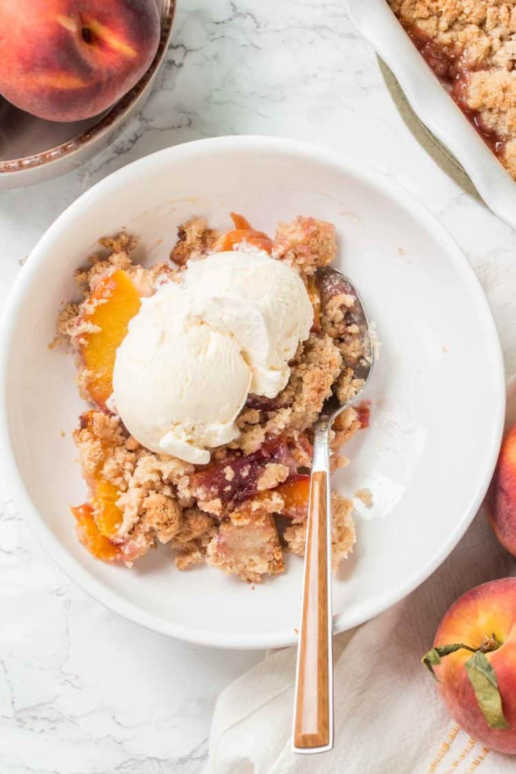 Easy peach cobbler in a a plate topped with vanilla ice cream and a spoon.