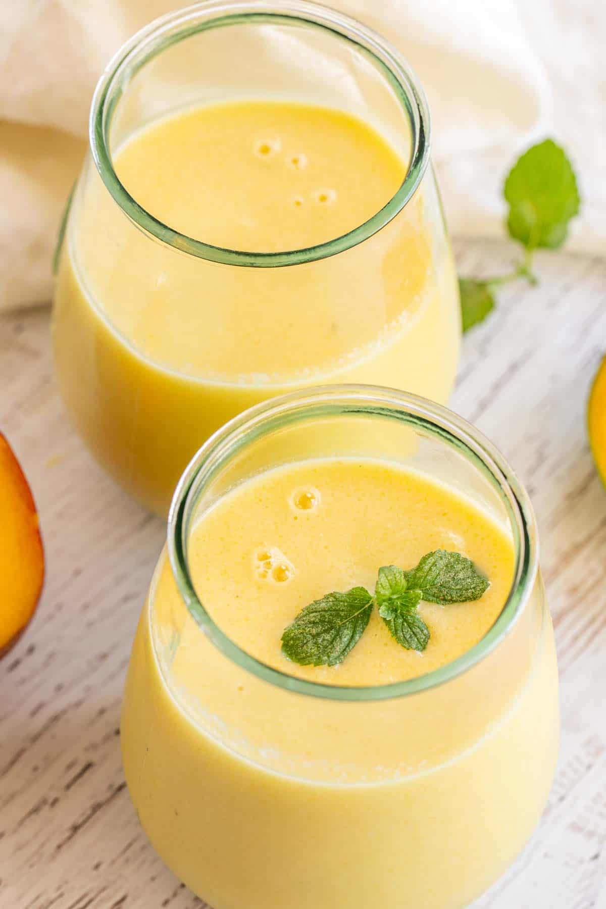 Two cups loaded with mango smoothie topped with mint. 