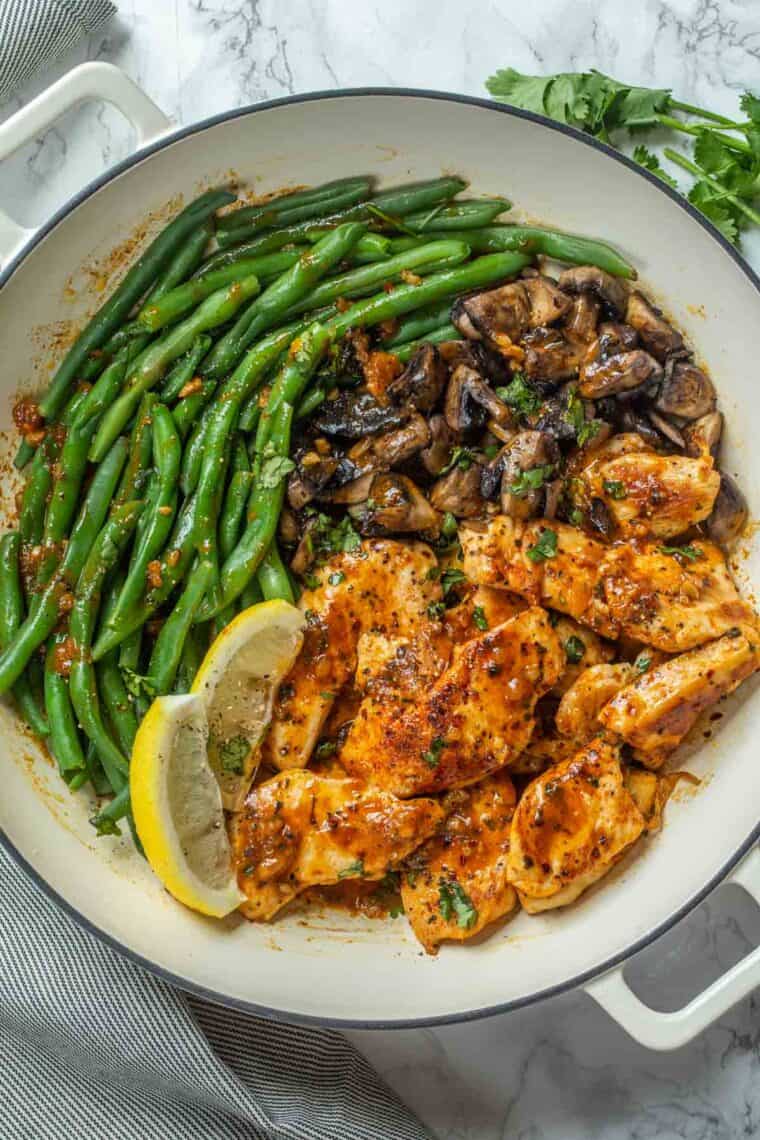 A white deep skillet loaded with lemon garlic chicken, green beans, and mushrooms. 