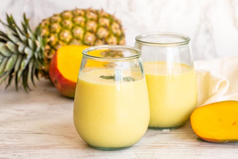 Pineapple mango smoothie in glass jars with fresh mint.