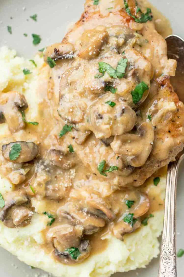Creamy mushroom sauce and pork chop with mashed potatoes on a plate with a spoon.