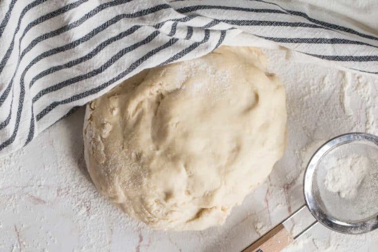 EASY homemade dough dusted with flour next to a sieve and a striped white rag.