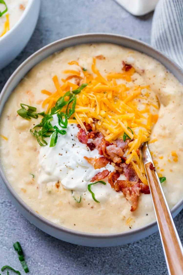 A bowl of potato soup topped with cheese, bacon and cheese, topped with green onions.