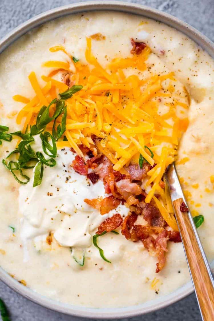 A bowl of creamy potato soup topped with cheese, bacon and sour cream. 