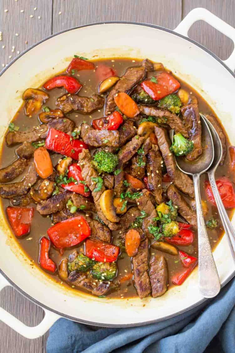 Simple beef stir fry recipe in a skillet with peppers, carrots, mushrooms, and broccoli topped with sesame seeds.