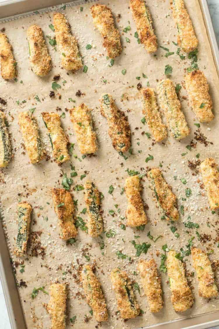 Baked Parmesan zucchini fries on a baking sheet topped with fresh greens and Parmesan cheese. 